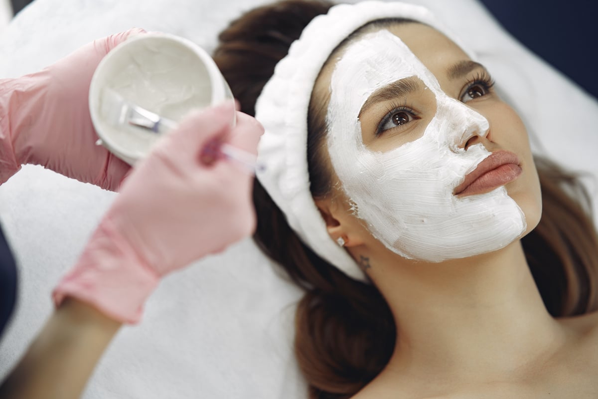 Crop unrecognizable beautician applying clay mask to clients face